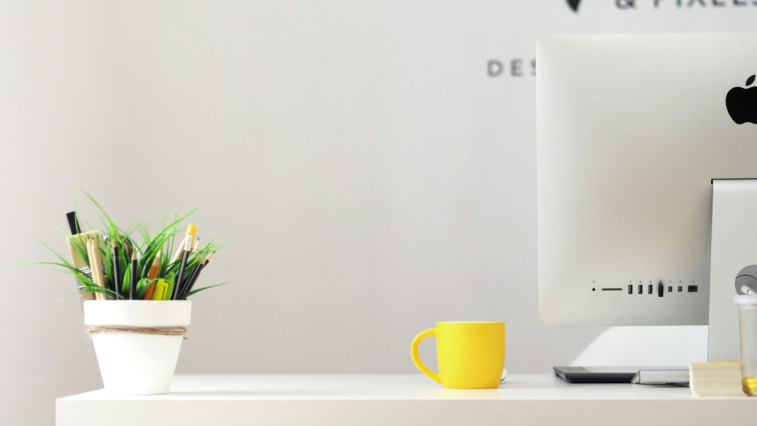 a desk with plant, yellow cup and a monitor